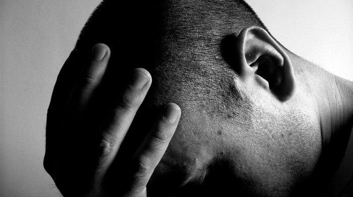 A man is holding his hand to his forehead looking down distressed. The image is black and white.