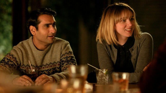 Emily Gardener, played by Zoe Kazan, is sitting beside Kumail Nanjiani ,playing himself, looking to something off screen.