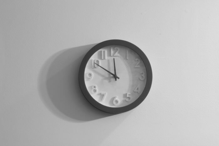 A grey image, showing a clock on the wall. The hour hand is on midnight, with the minute hand being 10 minutes to 12.